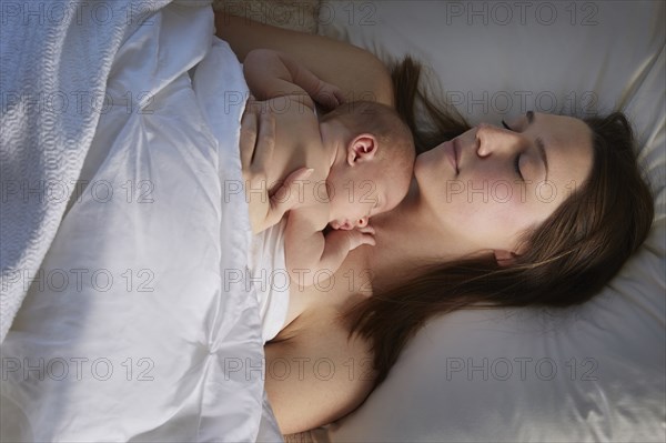 Mother sleeping with newborn baby on bed