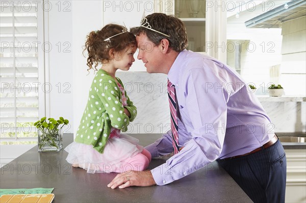 Caucasian father and daughter wearing tiaras in kitchen