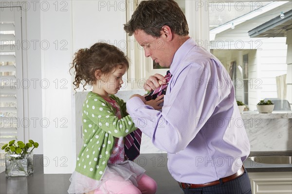 Caucasian girl tying necktie of father in kitchen