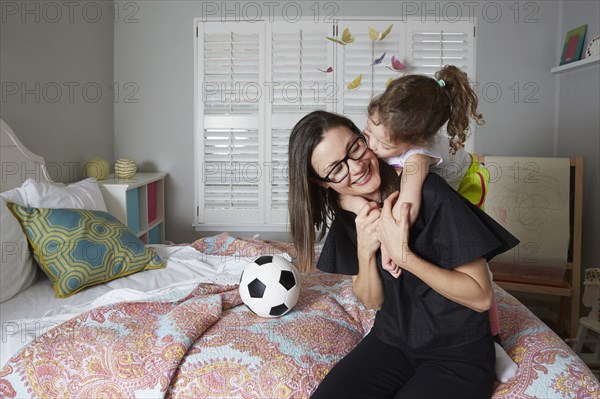 Caucasian mother and daughter kissing in bedroom