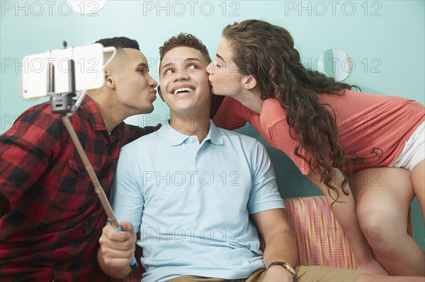 Smiling friends taking selfie kissing cheeks of man