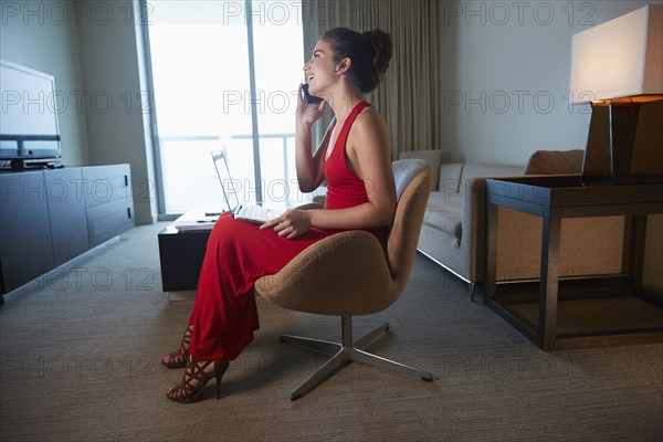 Mixed race woman in evening gown using laptop and cell phone