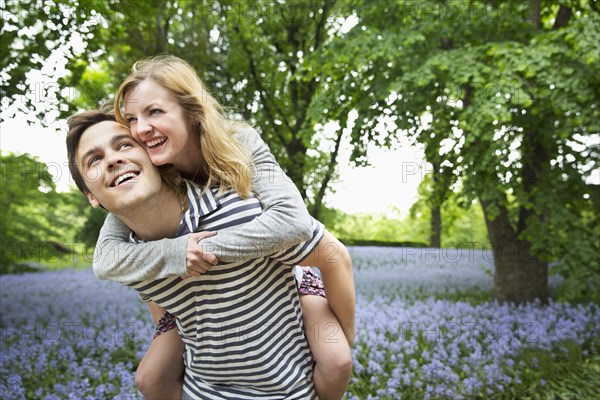 Caucasian man carrying girlfriend piggyback in field of flowers