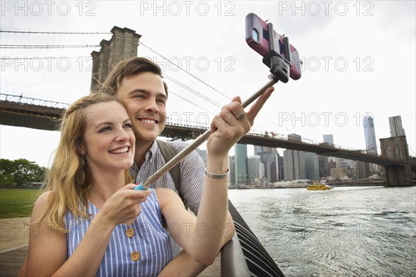 Caucasian couple taking selfie with cell phone under Brooklyn Bridge