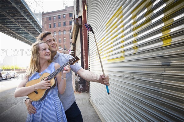 Caucasian couple taking selfie and playing ukulele in city