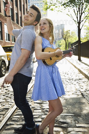 Caucasian couple playing ukulele on city street
