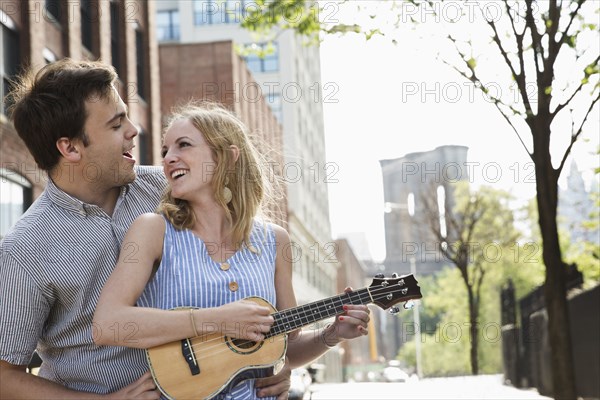 Caucasian couple playing ukulele in city