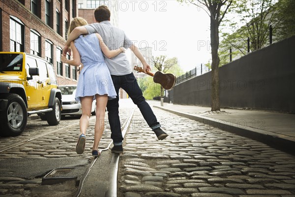 Caucasian couple carrying ukulele on city street