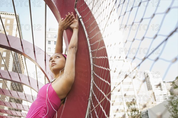 Hispanic woman listening to headphones under structure