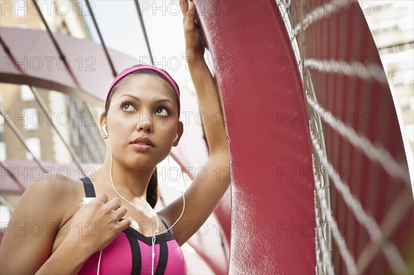 Hispanic woman listening to headphones under structure