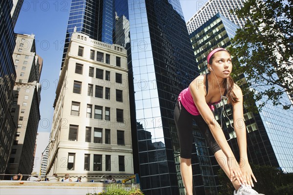 Hispanic woman stretching under highrise buildings