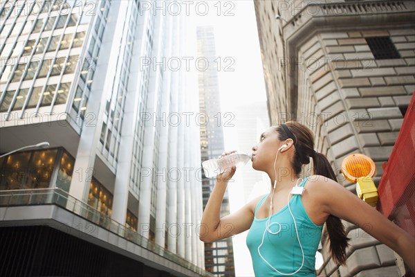 Hispanic woman drinking water bottle under highrise buildings