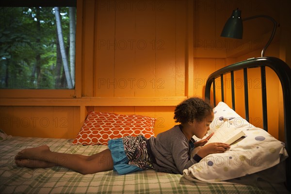 Mixed race girl reading on bed