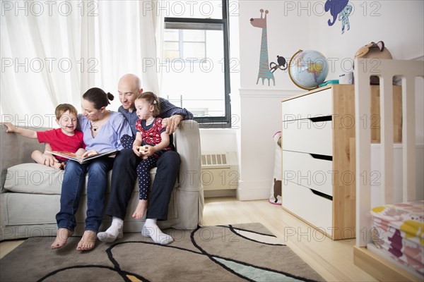 Family reading book on sofa in bedroom