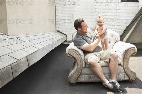 Caucasian father and baby daughter sitting in armchair outdoors