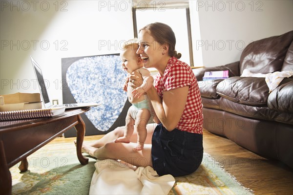 Caucasian mother and baby daughter using laptop in living room