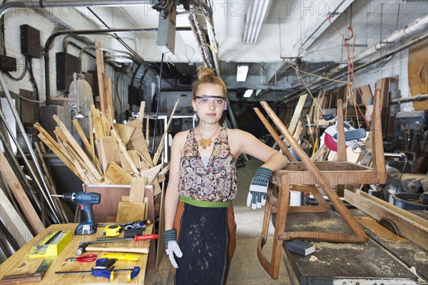 Caucasian woman leaning on wooden chair in workshop