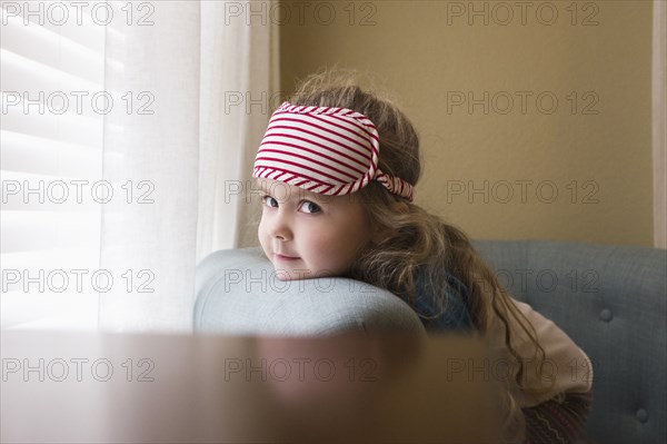 Caucasian girl resting chin on sofa near window