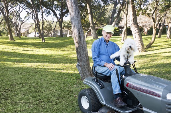 Older Caucasian man on riding lawnmower with pet dog