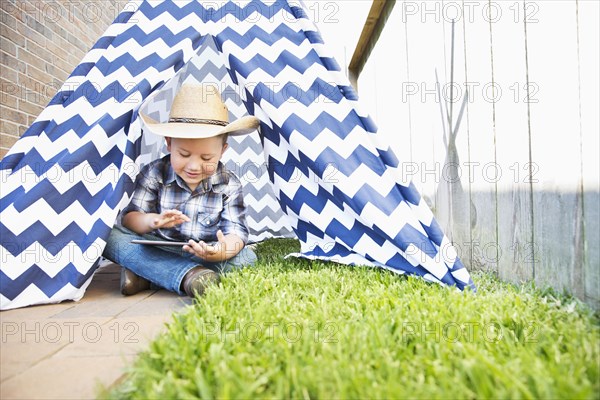 Caucasian boy wearing cowboy hat in teepee using digital tablet