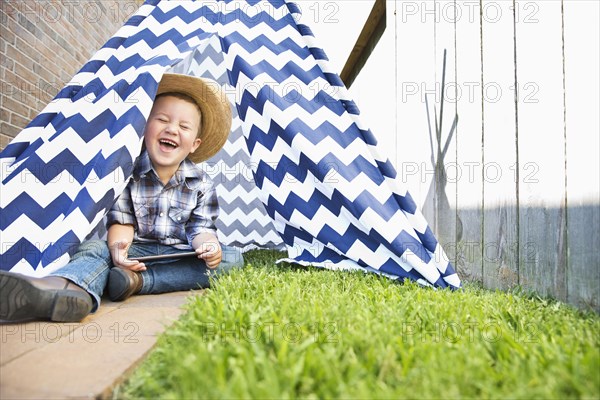 Caucasian boy wearing cowboy hat in teepee using digital tablet