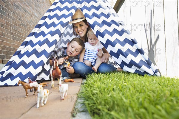 Caucasian mother and children in teepee playing with toy horses