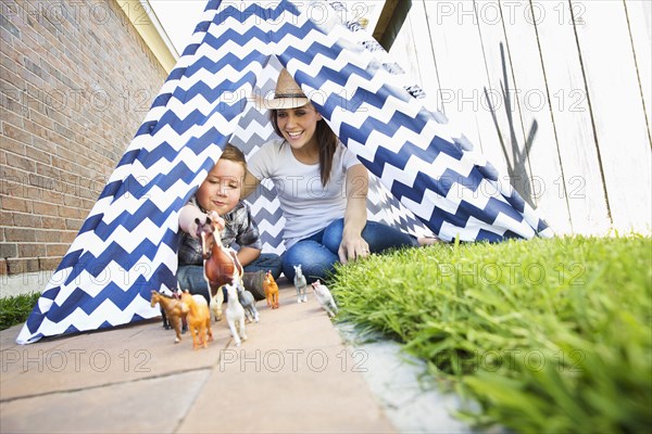 Caucasian mother and son in teepee playing with toy horses