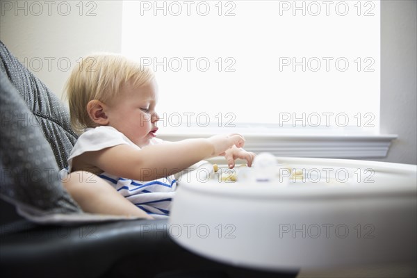 Caucasian baby girl self-feeding in high chair