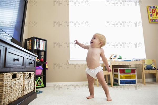 Caucasian baby girl standing and watching television