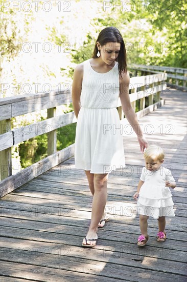 Caucasian mother and baby daughter walking on wooden footbridge
