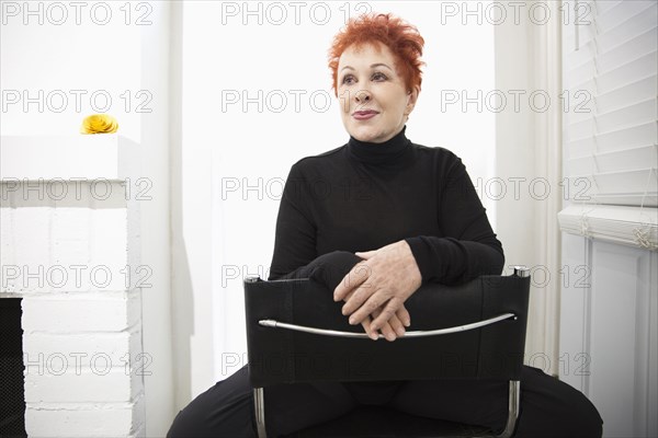 Older Caucasian woman wearing black turtleneck straddling chair