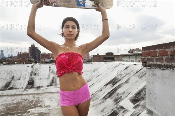 Mixed Race couple woman on rooftop holding skateboard