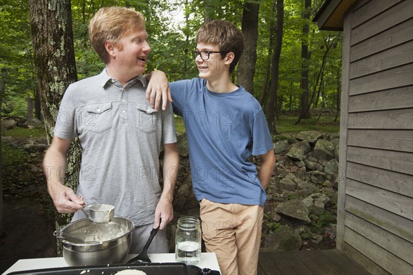 Caucasian son leaning on father cooking pancakes outdoors
