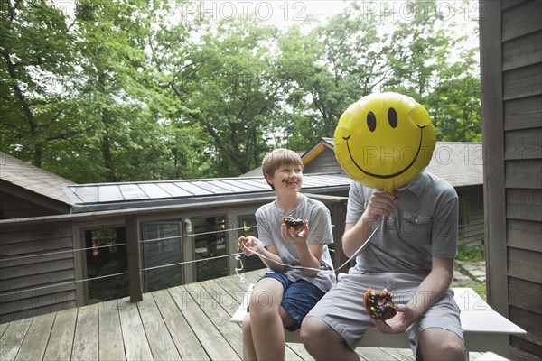 Caucasian father and son eating donuts with smiley face balloon