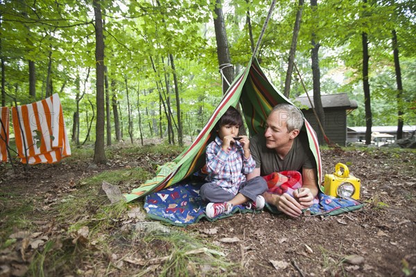 Father watching son playing harmonica in blanket fort