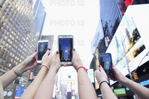 Arms of Caucasian women photographing skyscrapers with cell phones