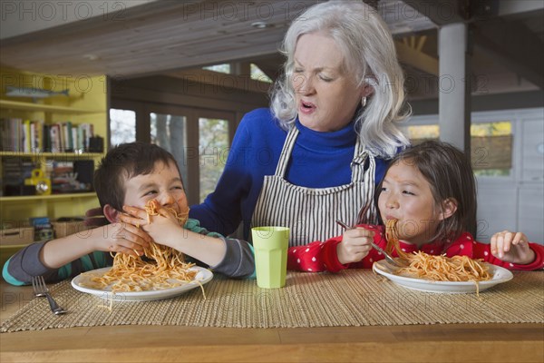 Grandmother watching grandson and granddaughter eat spaghetti