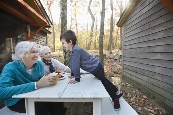 Grandmothers enjoying breakfast outdoors near cabin with grandson