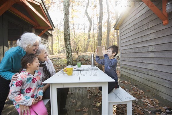 Grandson photographing grandmothers and sister with digital tablet