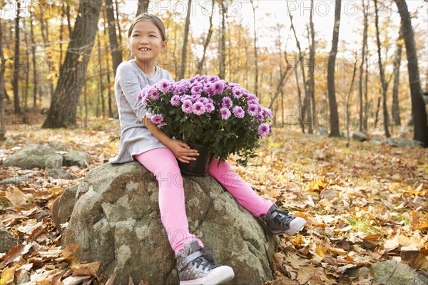 Smiling Mixed Race girls sitting on rock in autumn holding flowers