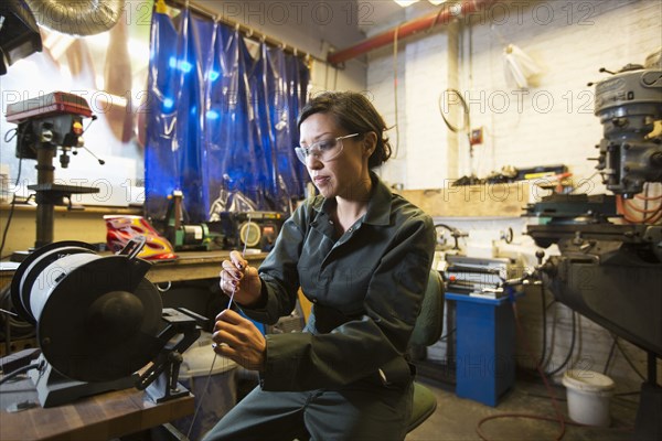 Mixed Race woman holding metal rod in workshop