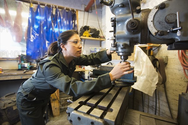 Mixed Race woman using machinery in workshop