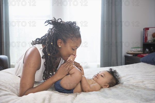 Mother kissing feet of baby daughter laying on bed