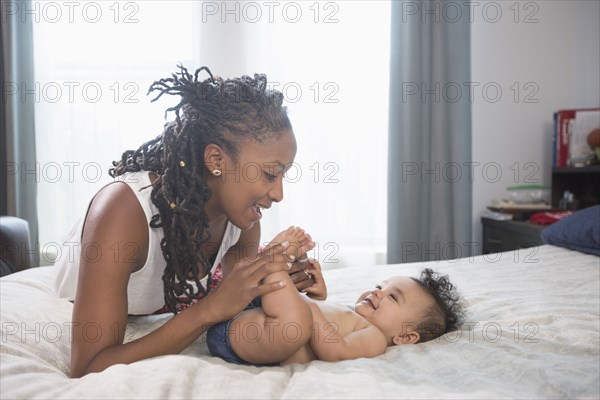 Mother playing with feet of baby daughter laying on bed