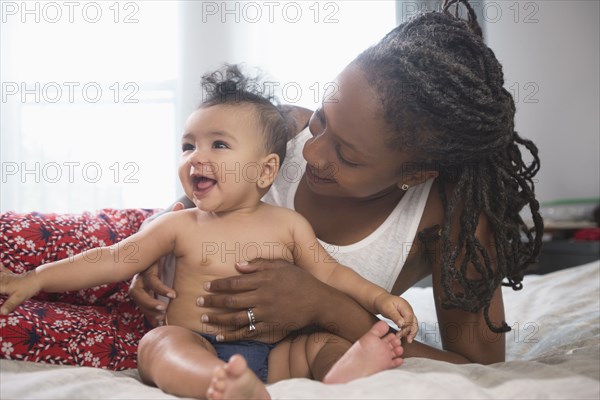 Mother holding smiling baby daughter on bed