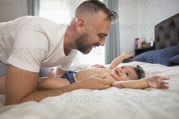 Father laying on bed playing with baby daughter