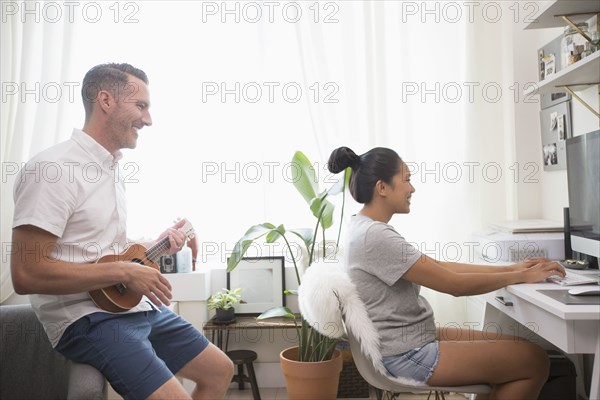 Man playing ukulele watching woman using computer