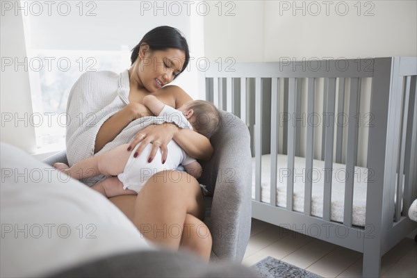 Woman sitting in armchair breast-feeding baby son