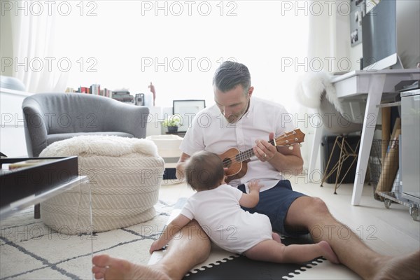 Father sitting on floor playing ukulele for baby son