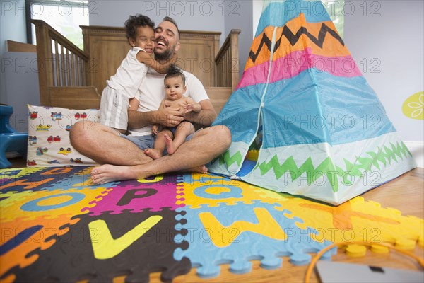 Father sitting on playroom floor holding son and daughter